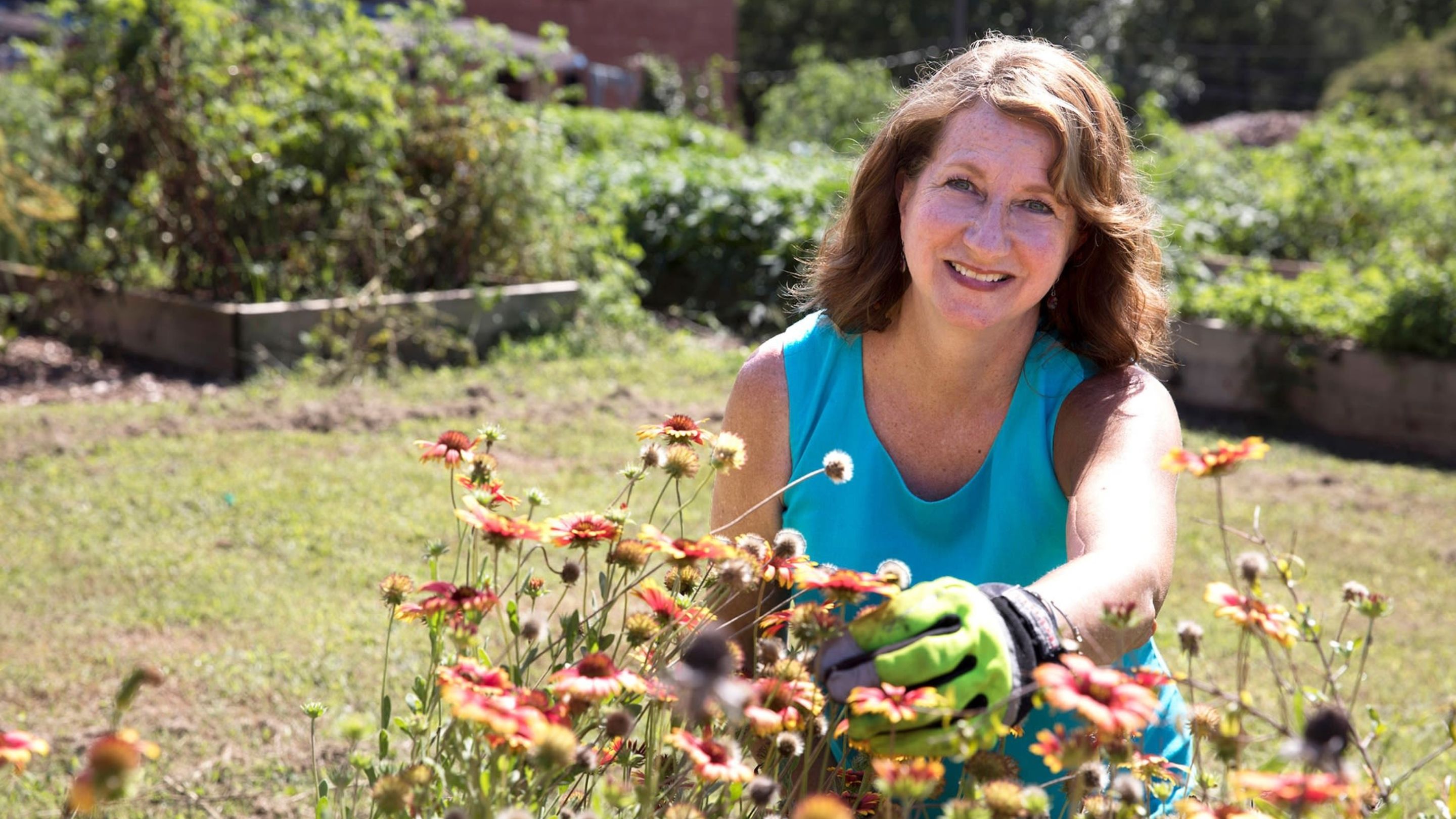 Smiling woman wearing gloves working in raised garden beds