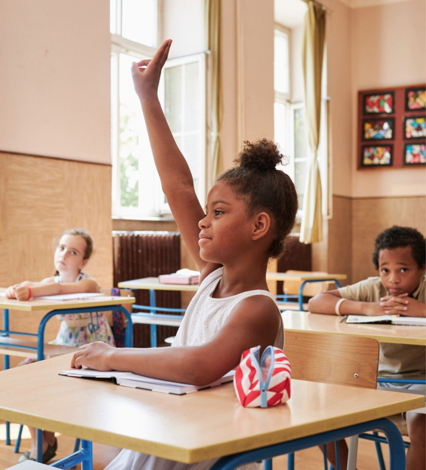 A young girl is raising her hand to get the teacher's attention in a classroom